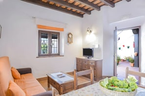 A room with a sofa, a small table, a TV on a wooden cabinet, and a window with a decorative grille.