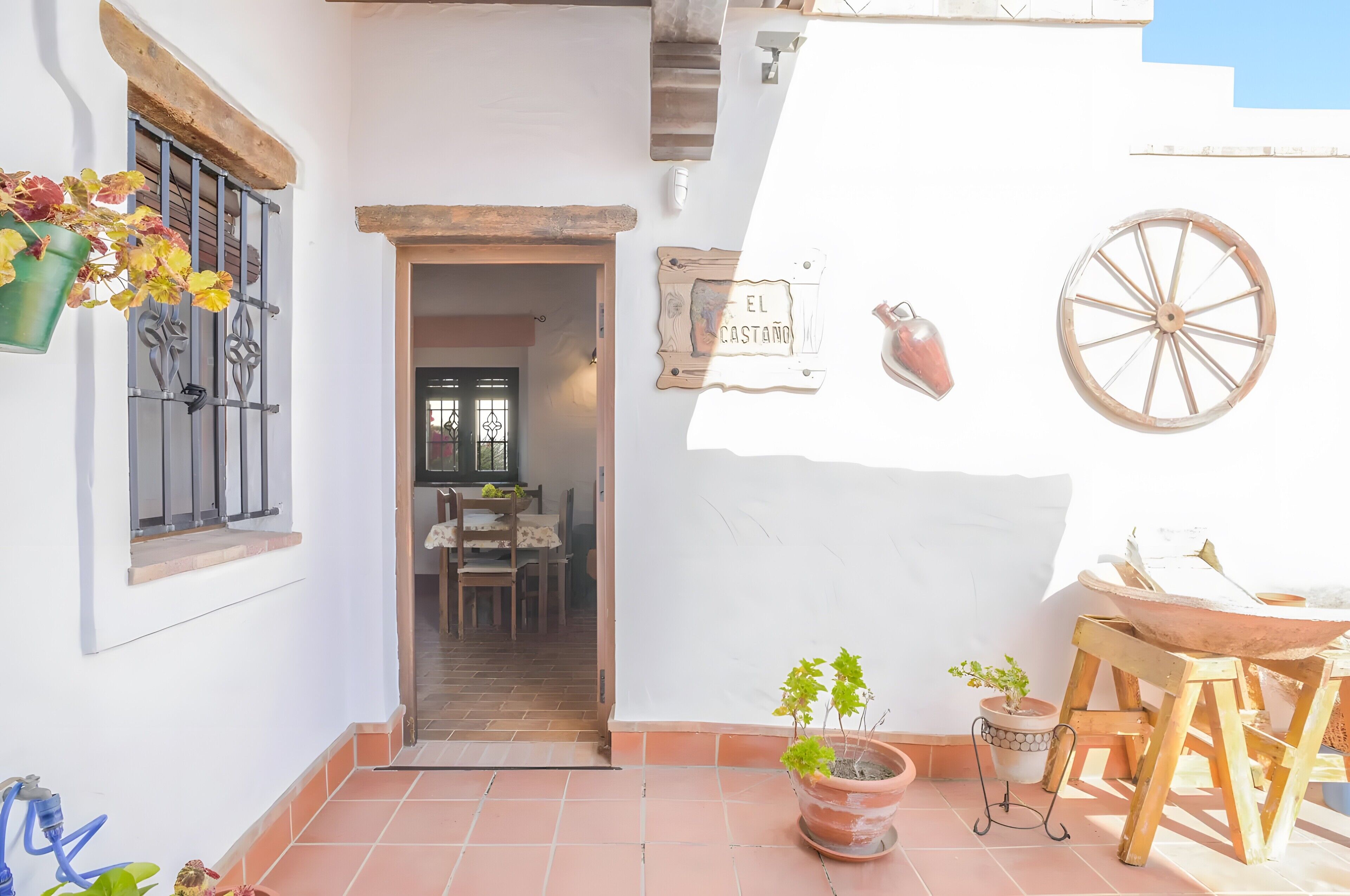 Un patio con una mesa, sillas, una maceta colgante, un letrero que dice 'EL CASTAÑO' y una rueda de madera.