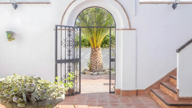 An arched entrance with a gate, a palm tree, and a potted plant. - Apartment 'Castaño' with Shared Pool, Wi-Fi and Air Conditioning (Barbate)