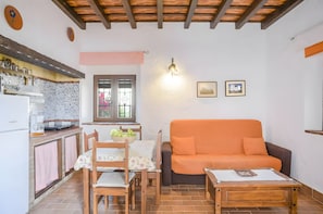 A compact living space with a kitchenette, a dining table with chairs, an orange sofa, and a small wooden table.