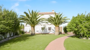 A white building with a tiled roof, surrounded by well-maintained grass and palm trees. - Apartment 'Castaño' with Shared Pool, Wi-Fi and Air Conditioning (Barbate)