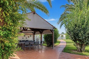 An outdoor patio with a covered seating area, a pathway, and surrounding greenery. - Apartment 'Castaño' with Shared Pool, Wi-Fi and Air Conditioning (Barbate)