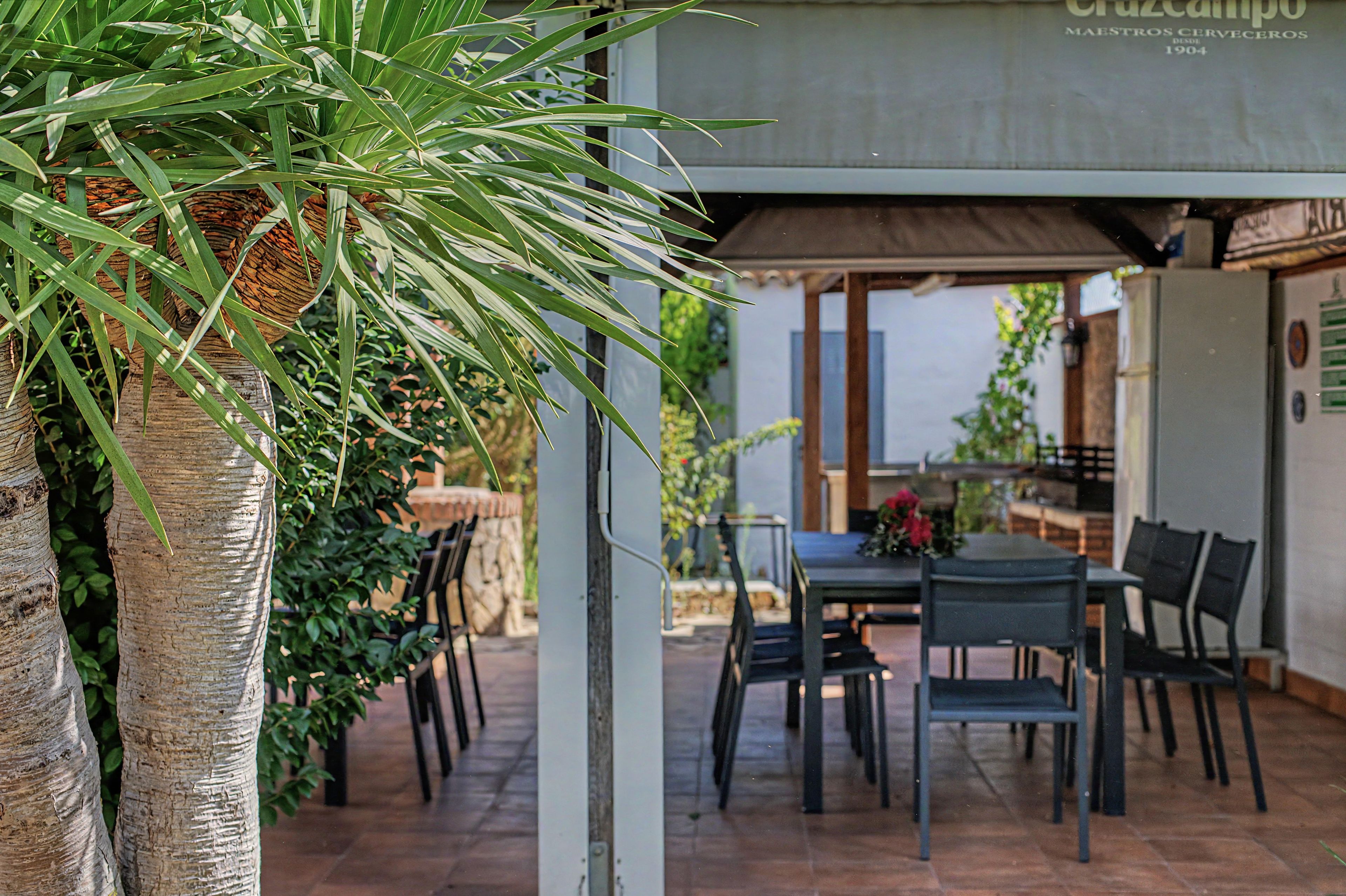 An outdoor patio area with a table and chairs, surrounded by greenery and a pergola structure.