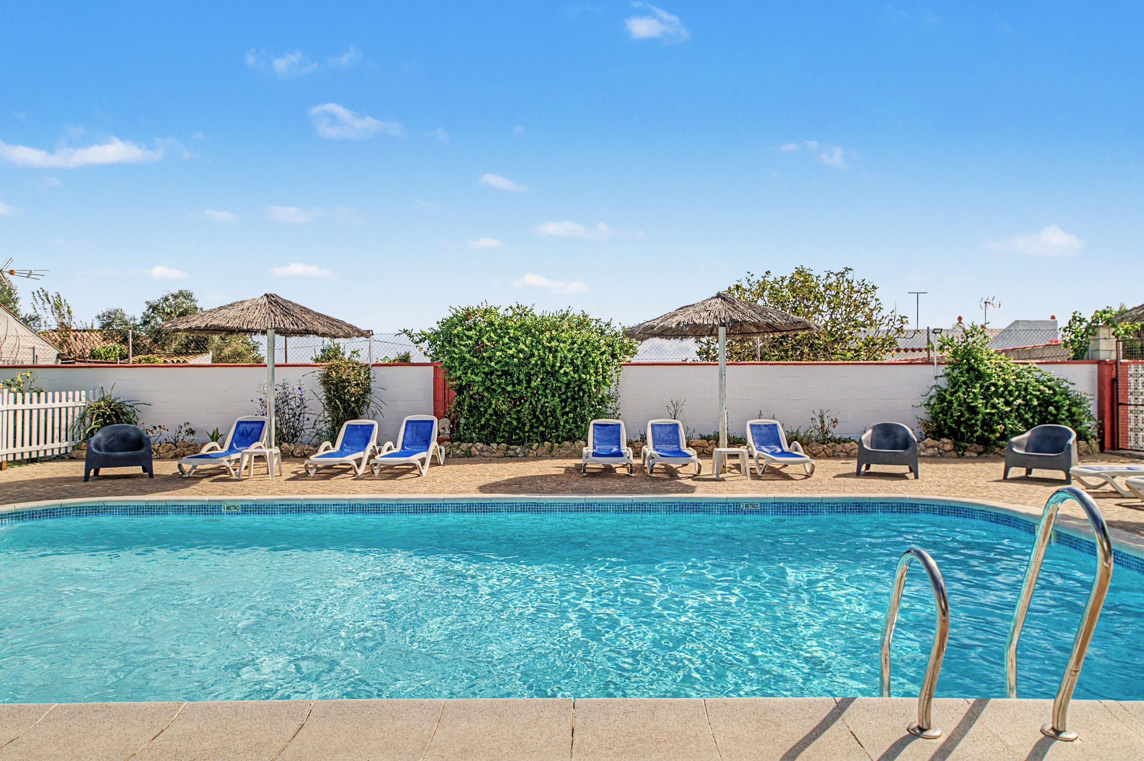 A swimming pool with clear blue water, surrounded by lounge chairs and a white wall.
