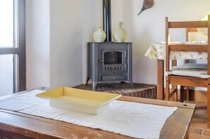 A room with a wooden table, a yellow tray, a white tablecloth, a wooden chair, and a gray wood stove.