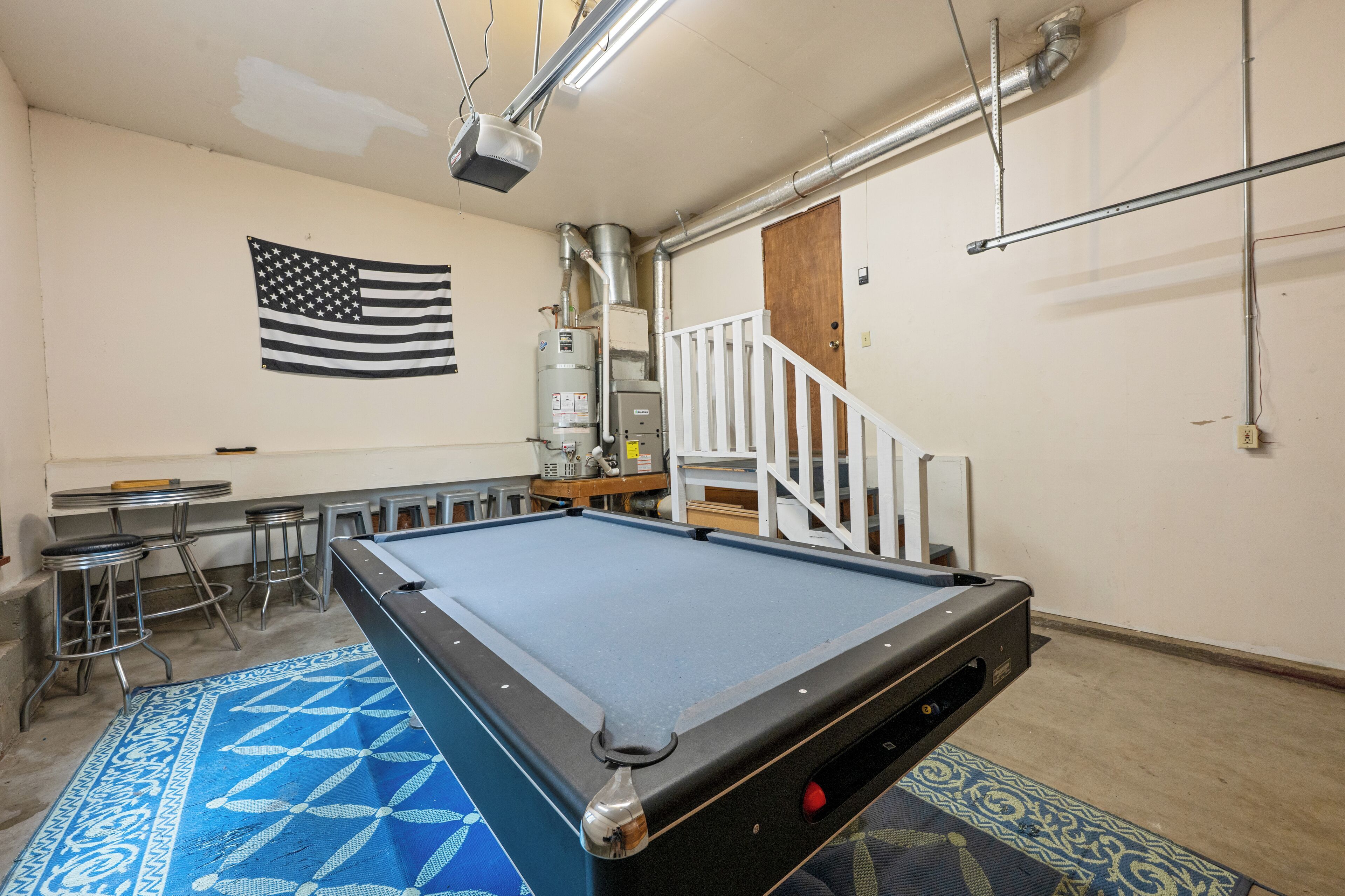 Ein Billardtisch in einem Raum mit einer Flagge an der Wand, einer Treppe und einer Bar mit Hockern.