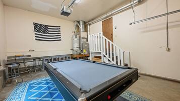 Ein Billardtisch in einem Raum mit einer Flagge an der Wand, einer Treppe und einer Bar mit Hockern.