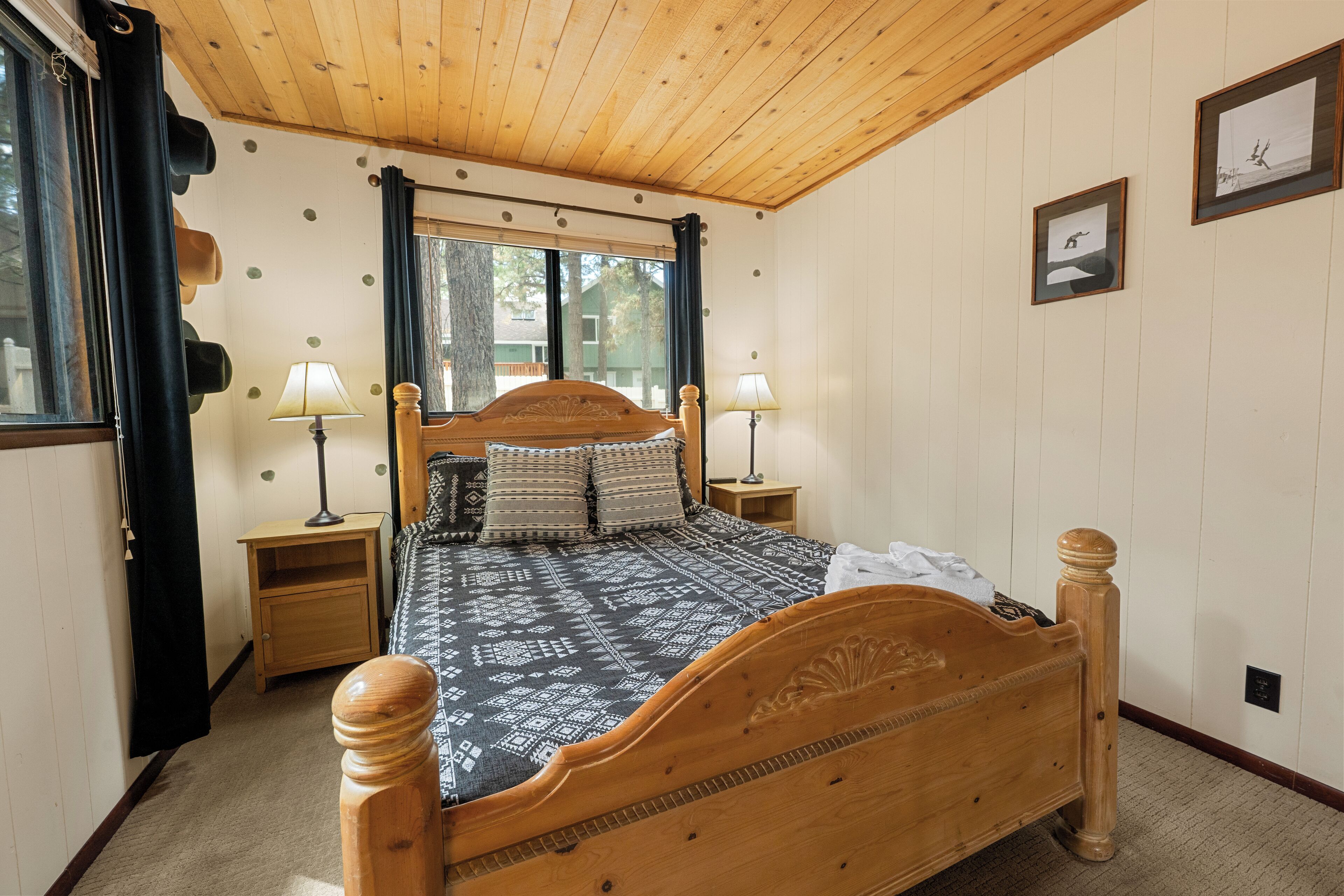 A wooden bed with a patterned bedspread, two bedside lamps, and a window with curtains.