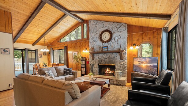 Una sala de estar acogedora con chimenea de piedra, vigas de madera, un sofá grande y un televisor.