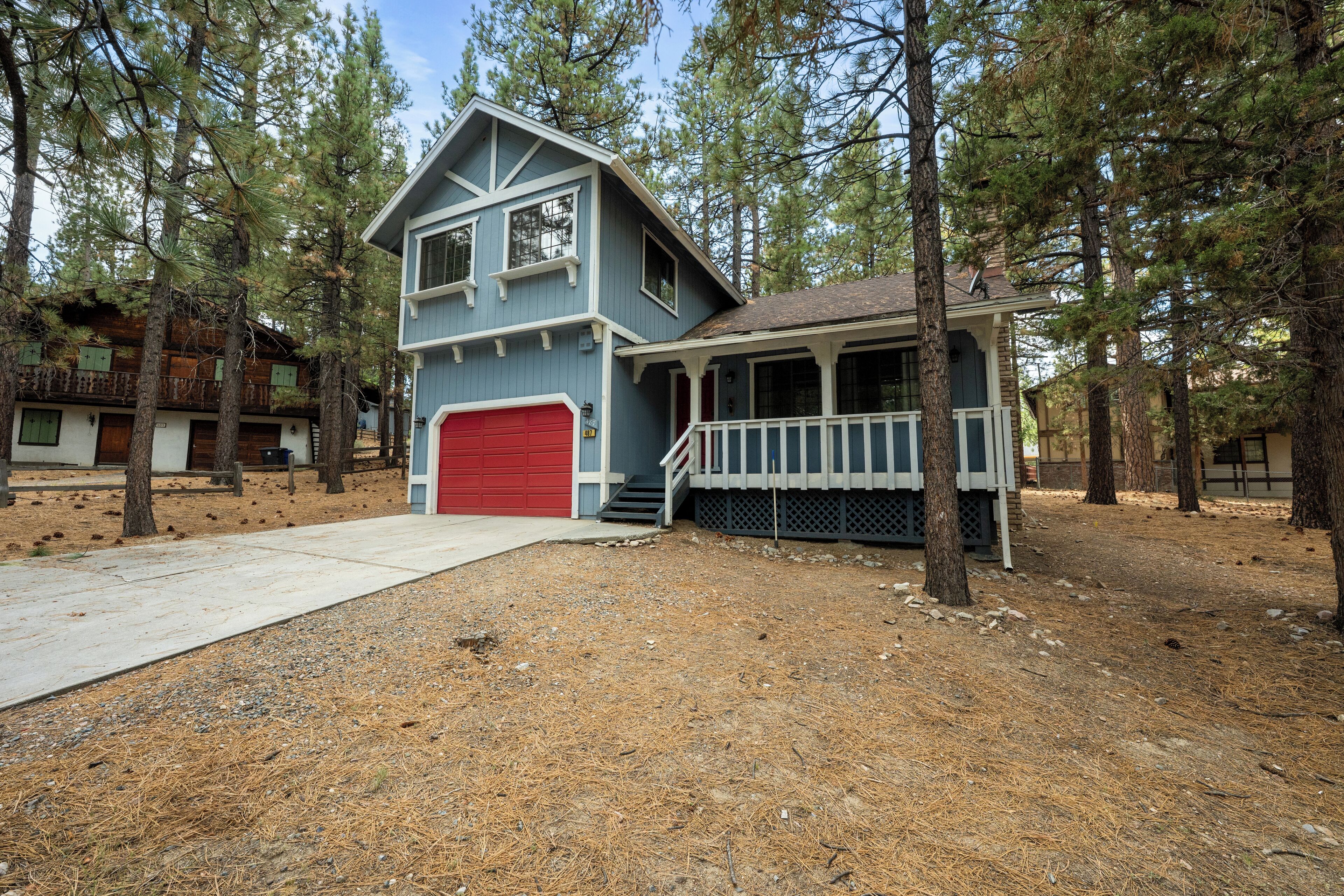 A two-story house with a red garage, a covered porch, and a small front yard with pine trees.
