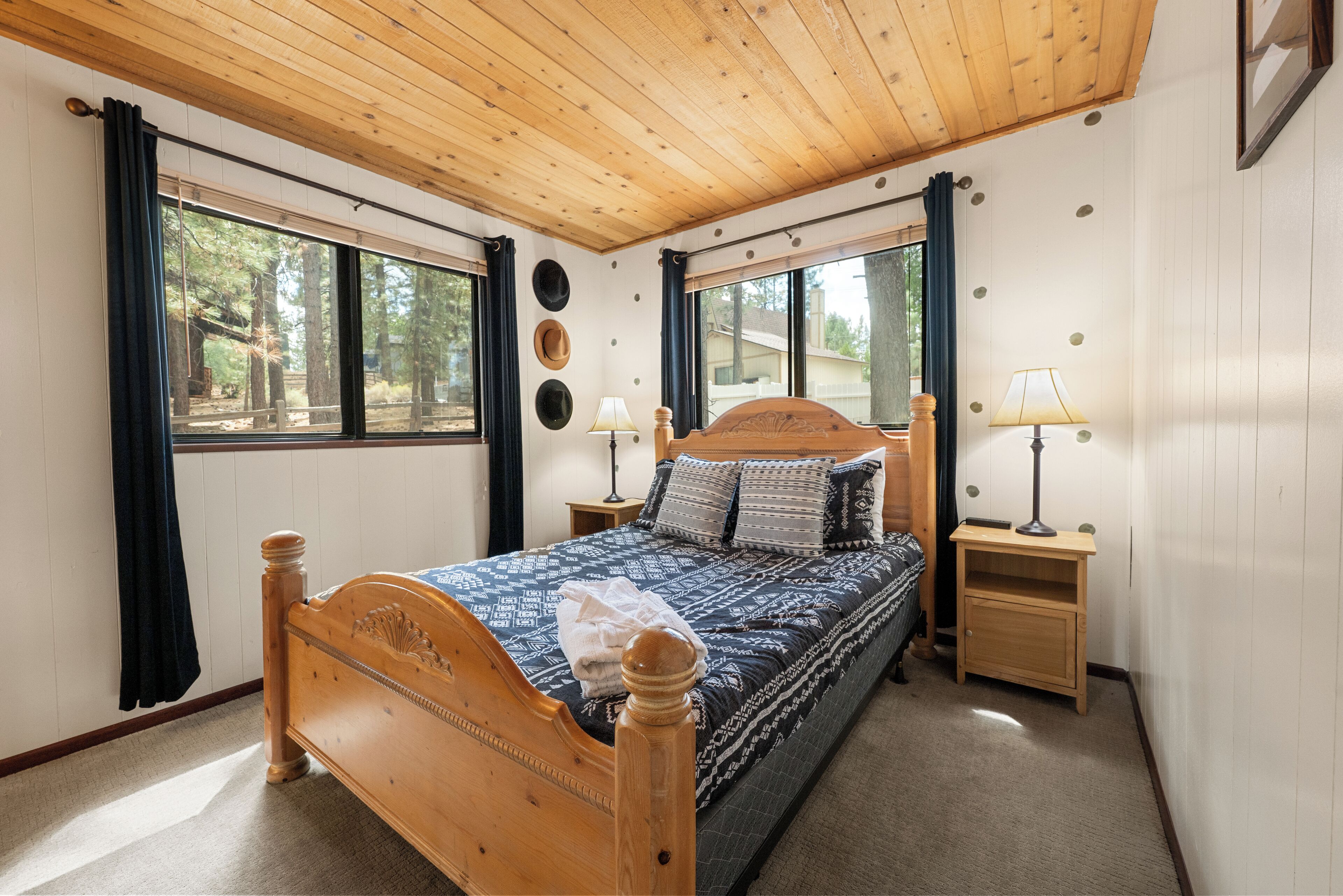 Un dormitorio con una cama de madera, dos mesitas de noche y un ventanal con cortinas.