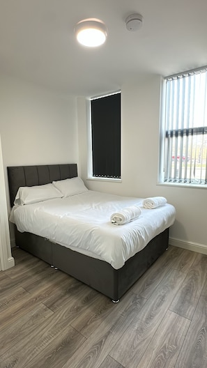 A neatly made bed in a room with a large window, a ceiling light, and a smoke detector. - Akai Manage (Scunthorpe)