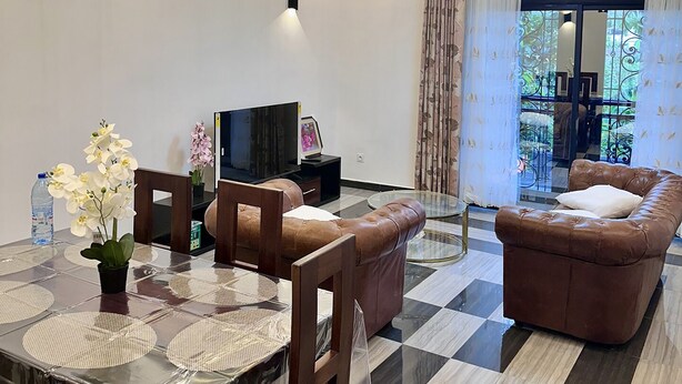 Sala de estar moderna com área de jantar, piso xadrez, sofás de couro e televisão.