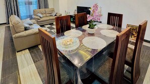 Uma sala de estar moderna com área de jantar, apresentando um conjunto de sofá, uma mesa de jantar com cadeiras e uma TV.