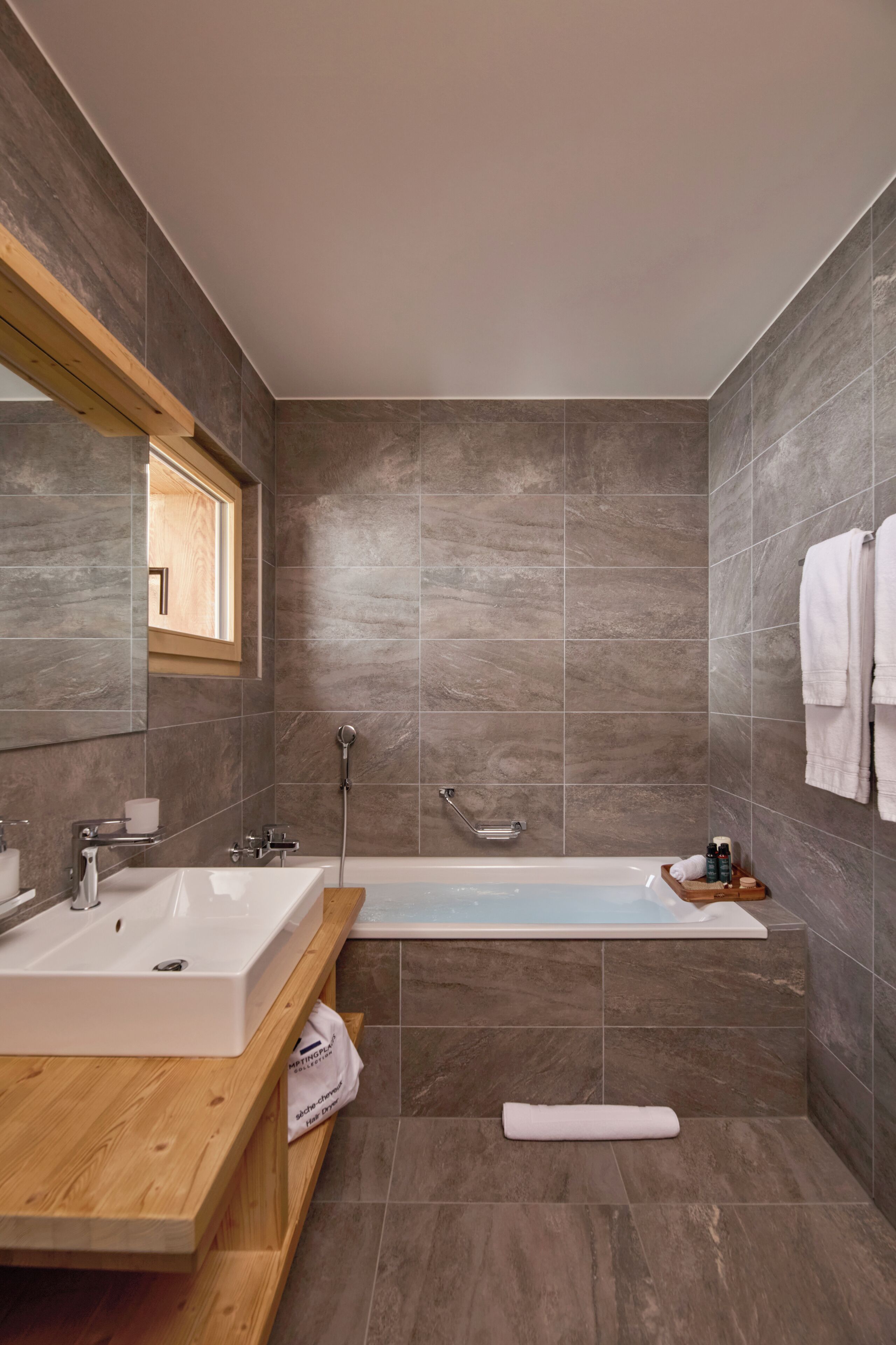 Une salle de bain moderne avec un grand miroir, deux lavabos, une baignoire et un meuble-lavabo en bois.