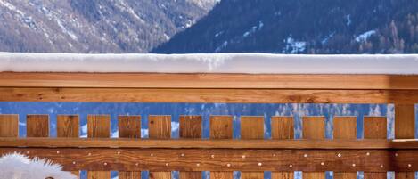 Une terrasse en bois avec une chaise et une petite table, d’où l’on peut admirer une chaîne de montagnes enneigées.