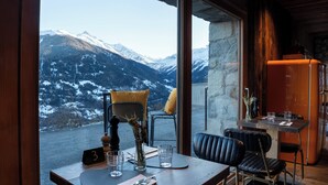Un comedor con una mesa lista para dos, vista a montañas nevadas y una pared de piedra.