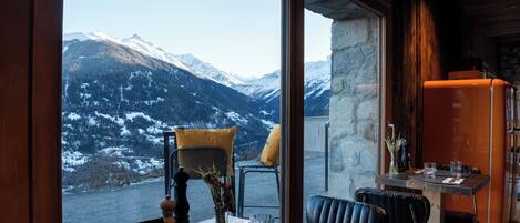 Un comedor con una mesa lista para dos, vista a montañas nevadas y una pared de piedra.