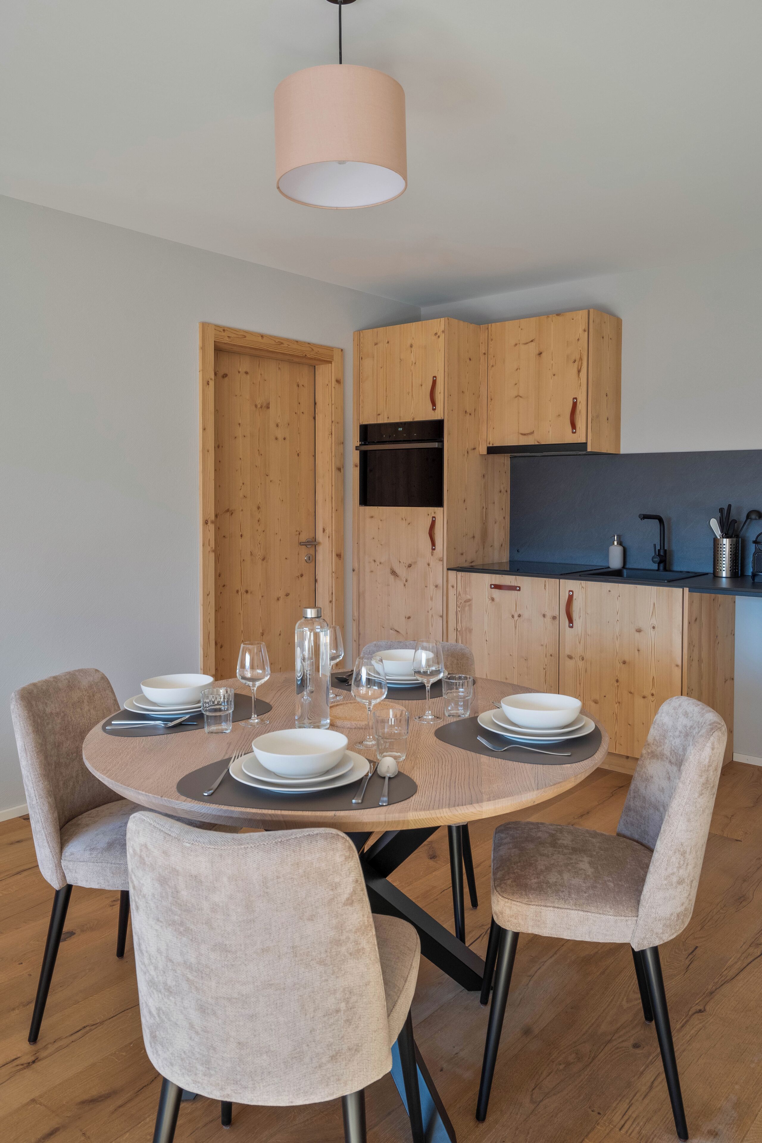 Un comedor con una mesa redonda dispuesta para cuatro, armarios de madera y una lámpara colgante moderna.
