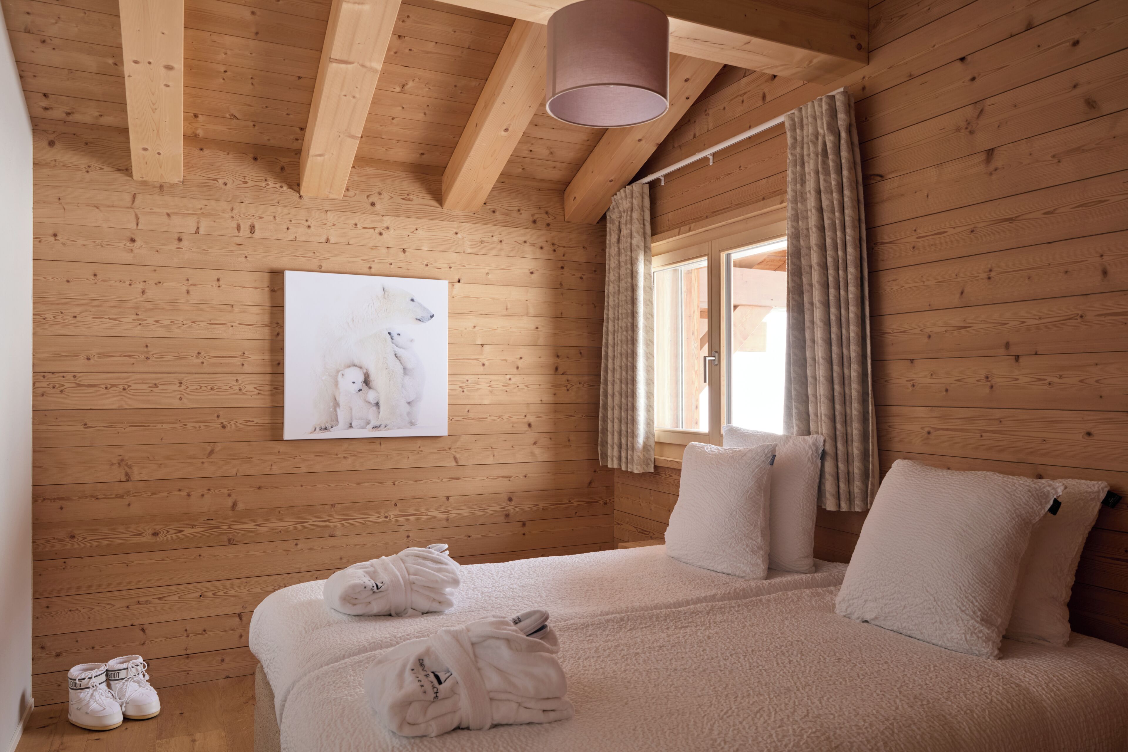 Een slaapkamer in een houten hutje, met een bed, handdoeken en een foto van een witte hond.