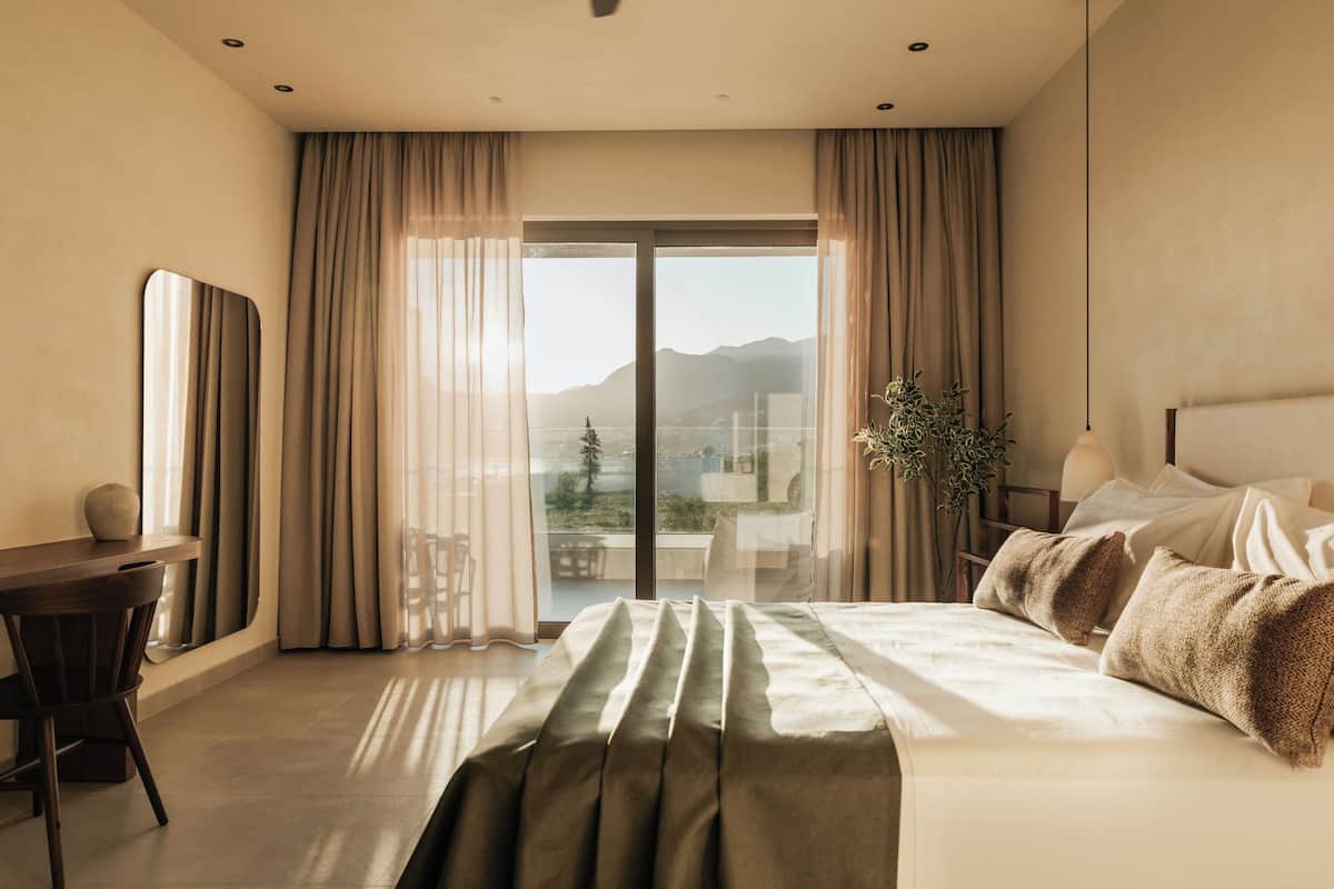 A modern hotel room with a large bed, a desk, and a view of mountains through the window.