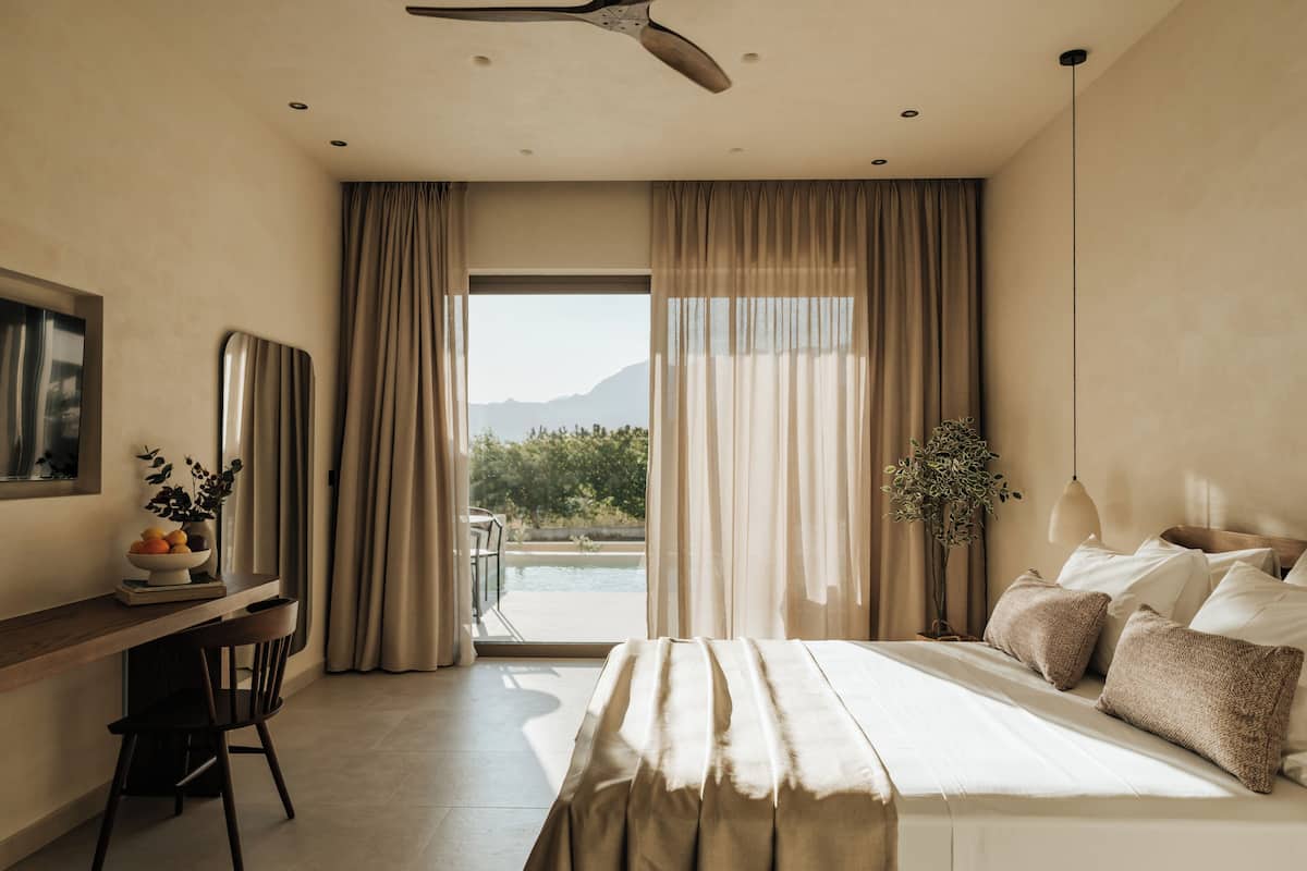 A bedroom with a bed, a desk, and a view of mountains through the window.