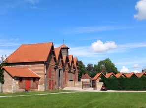 Un bâtiment traditionnel en briques, avec un toit recouvert de tuiles rouges, une clôture en bois et un parterre d’herbe à l’avant.