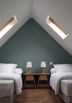 Une chambre avec deux lits, un plancher en bois et un plafond en pente doté de fenêtres de toit.
