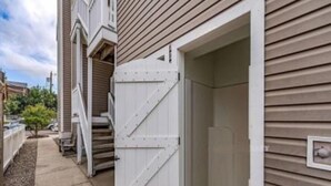 En boligbygning med en garageport åben, der viser et overdækket udendørs område med en haveslange og et lille træ.
