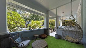 A covered porch with artificial grass, wicker furniture, and a hanging chair. - Midtown 2BR | Walk to Piedmont Park + Beltline (Atlanta)