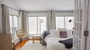 Une chambre à coucher avec un lit, une chaise, une commode et de grandes fenêtres.