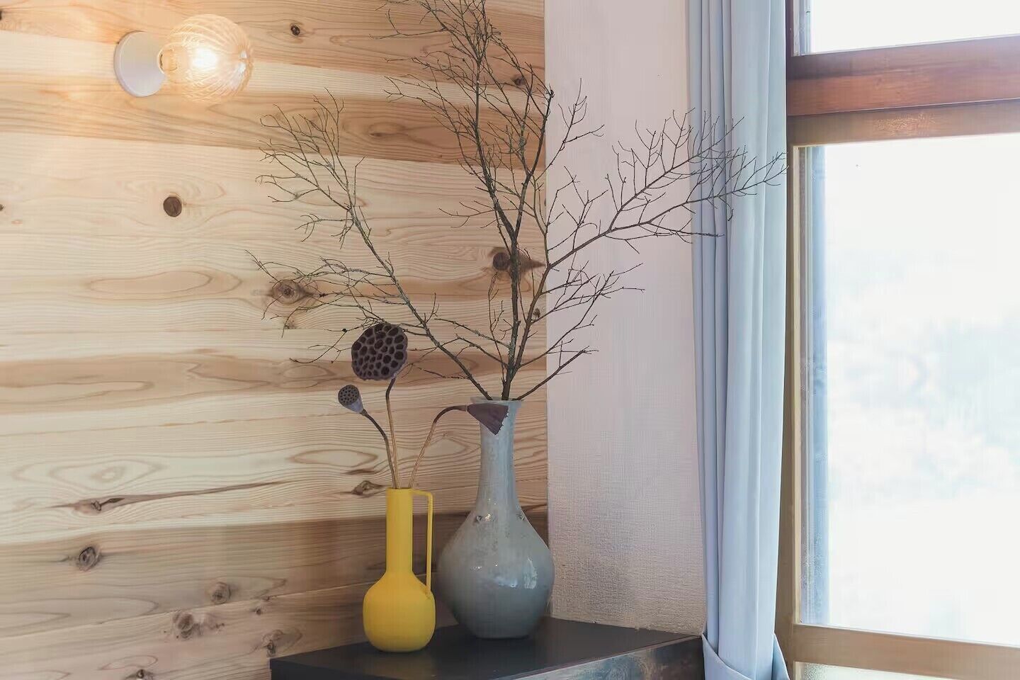 A wooden wall with a window and two vases on a shelf.