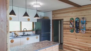 A modern kitchen with pendant lights, a built-in refrigerator, and a wooden wall with skateboards.