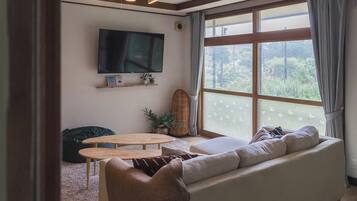 A living room with a large window, a flat-screen TV, a sofa, a coffee table, and a chair.