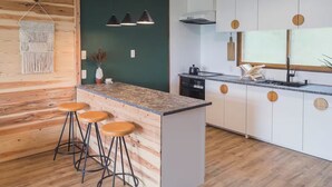 A modern kitchen with a wooden island, bar stools, pendant lights, and a built-in oven.
