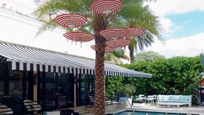 Un espace aménagé au bord de la piscine, avec un palmier, des parasols à rayures et des sièges d’extérieur.