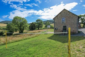 A stone building with a door and window, surrounded by a grassy field and trees.