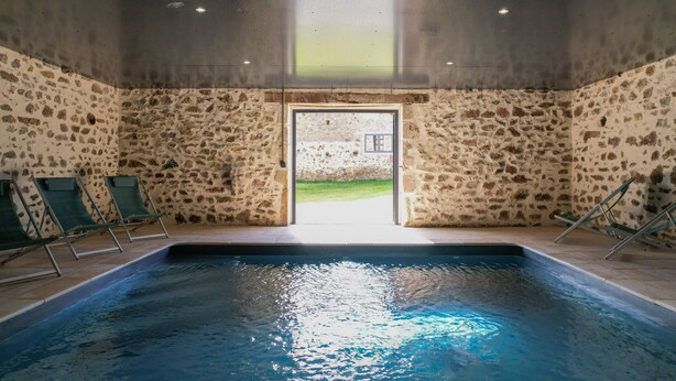 An indoor swimming pool with stone walls, a clear view outside, and a door leading to an outdoor area.