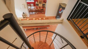 A spiral staircase with a wooden finish and metal railings, leading to a dining area with a long table and chairs.