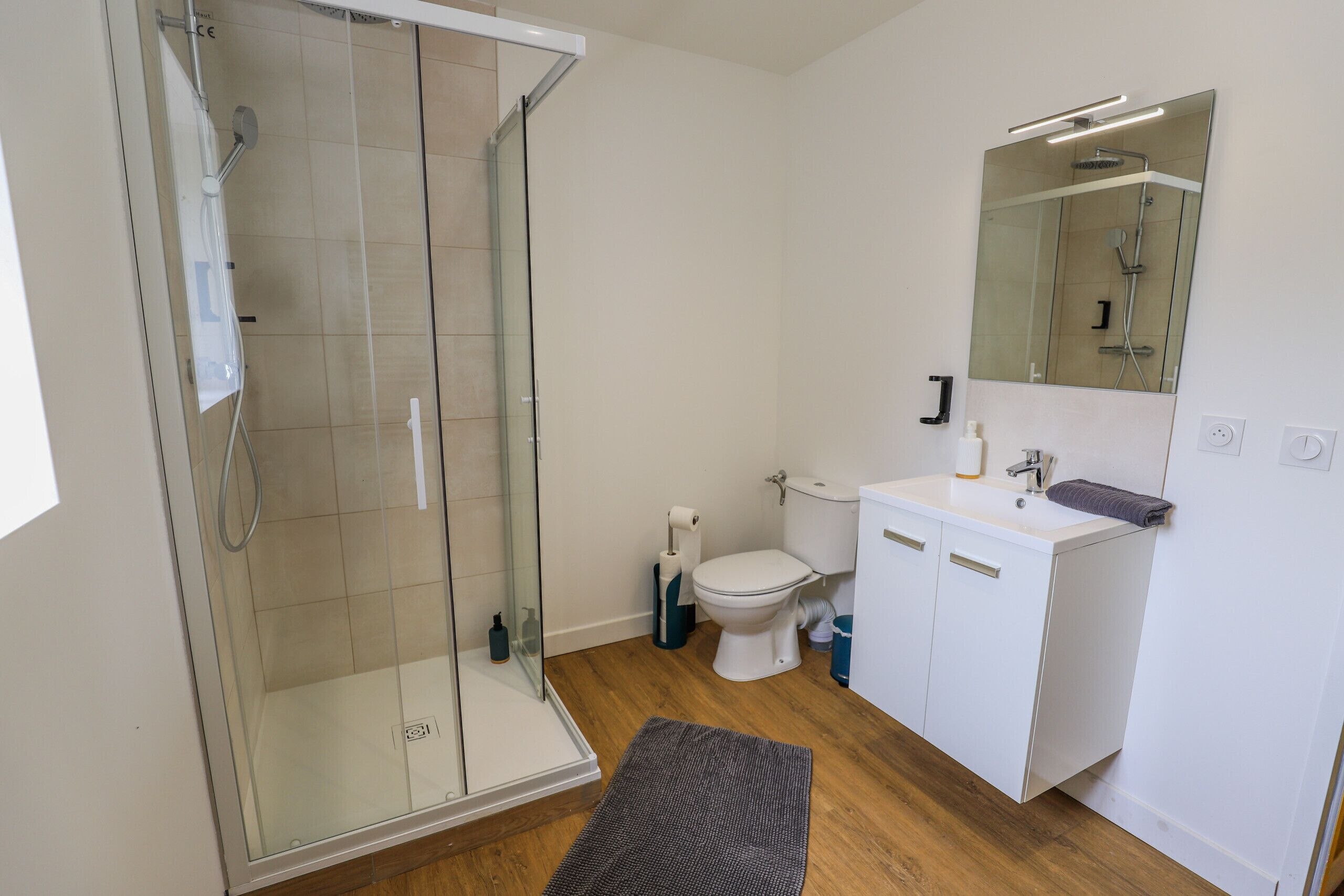 Une salle de bain moderne avec une douche à parois de verre, des toilettes blanches et un lavabo avec un miroir au-dessus.