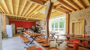 Un comedor amplio con mesas y bancos de madera, una cocina al fondo y ventanas grandes que dejan entrar la luz natural.