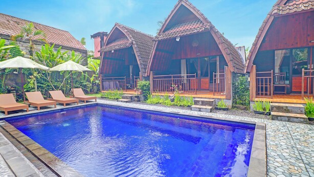 A swimming pool with lounge chairs and wooden cabins with tiled roofs. - OYO 94782 Loka Loka Ubud (Ubud)