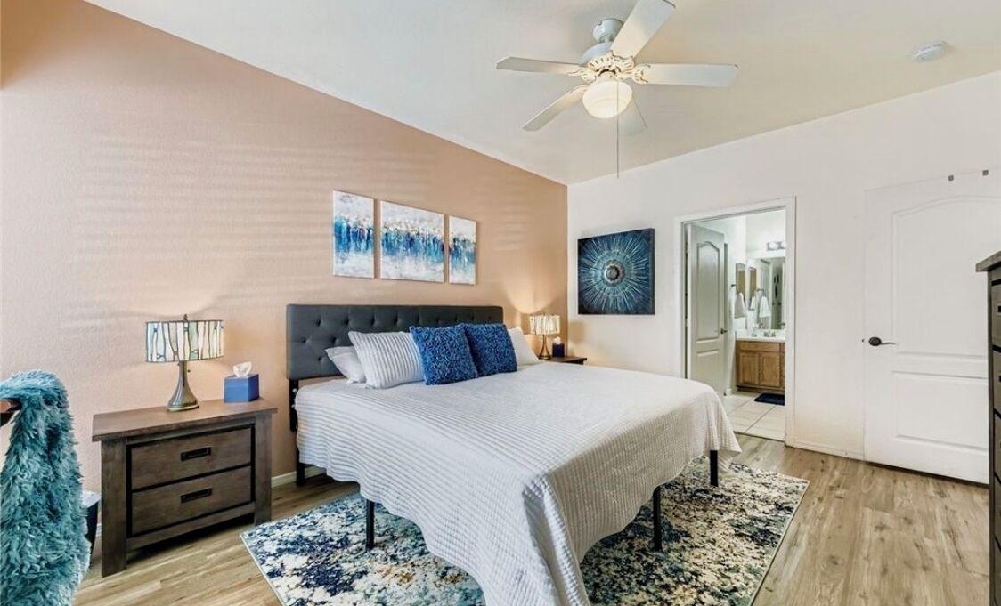 A bedroom with a bed, nightstands, a lamp, a ceiling fan, and artwork on the walls.