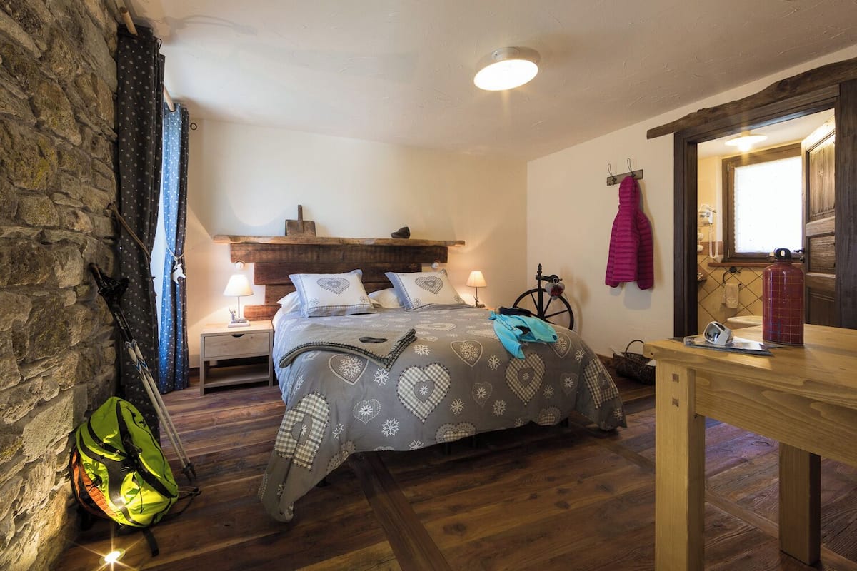 Ein gemütliches Schlafzimmer mit Bett, Holz-Kopfteil, Steinwand und einem Holztisch.