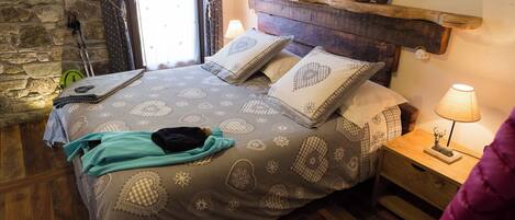 A cozy bedroom with a stone wall, a wooden headboard, and a nightstand with a lamp.