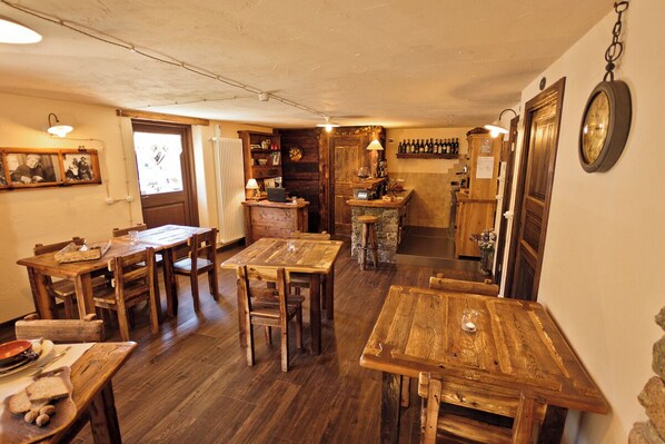 Un comedor rústico con mesas y sillas de madera, una zona de bar con botellas y una encimera de piedra.
