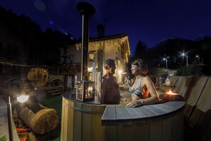 A wooden hot tub with a stone structure in the background, surrounded by outdoor lighting. - La Maison d'Antan (Bionaz)