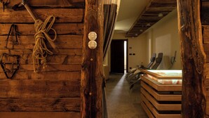 Un intérieur rustique en bois, avec des cordes et des outils en métal accrochés au mur, un lit doté d’une tête de lit en bois, et un couloir menant à une autre pièce.