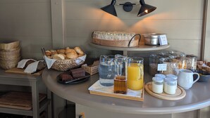 Un bufé de desayuno con pan, bollería y bebidas sobre una mesa.
