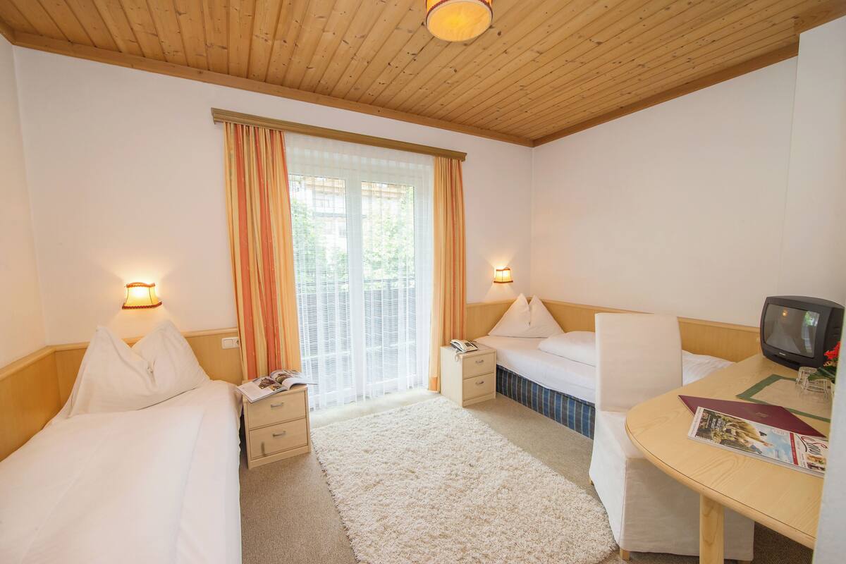 Habitación de hotel con dos camas, un escritorio, televisor y ventana con cortinas.